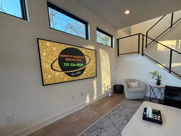 Wall-mounted TV displaying the Austin TV Mounting Service ATX logo in a bright living room.